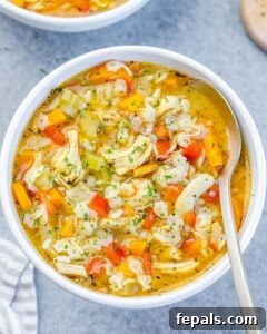 A serving of chicken pastina soup garnished with fresh chopped parsley.