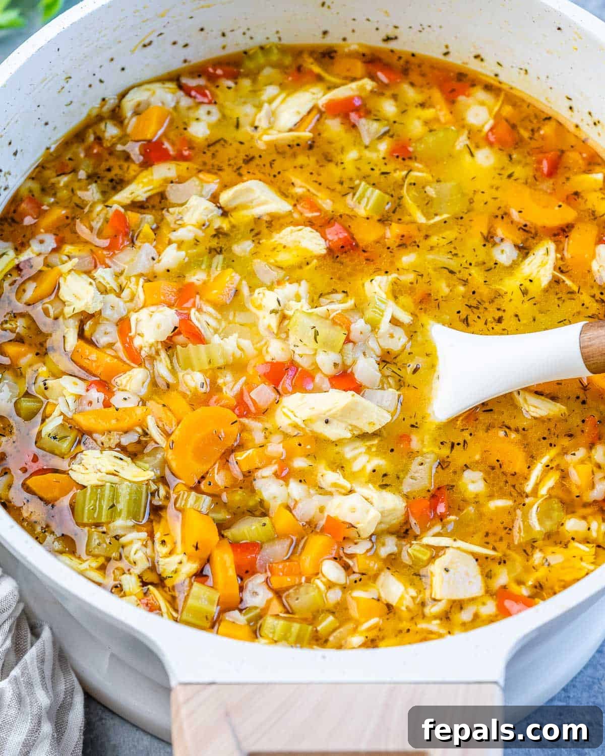 A white pot of chicken pastina soup with a serving spoon, ready to be dished out.