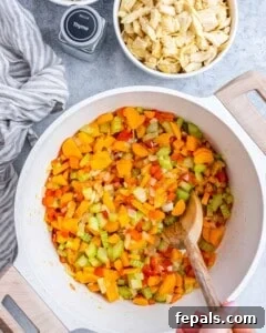 Sautéing diced vegetables (onion, celery, carrots, bell pepper, garlic) in olive oil in a soup pot.
