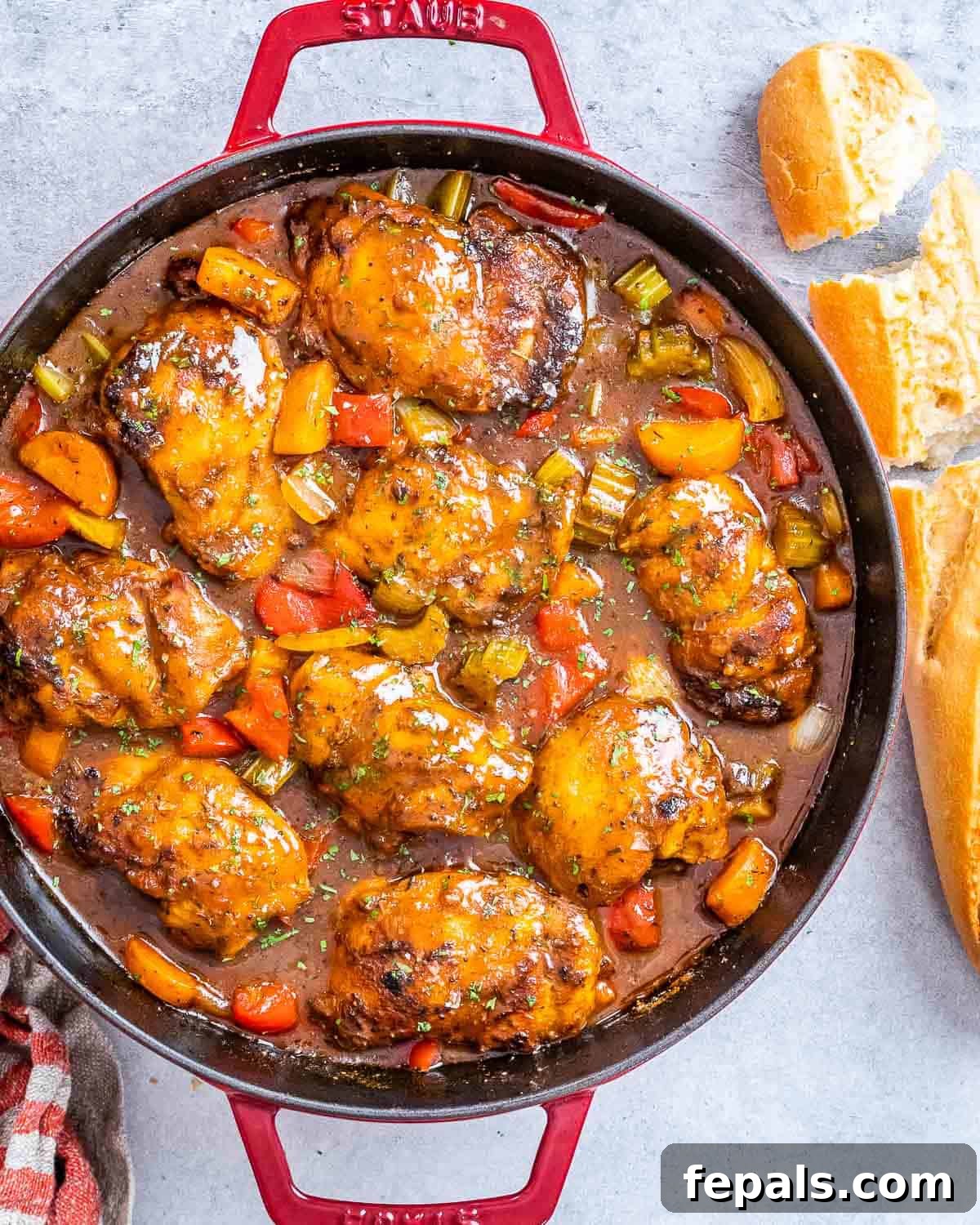 Classic Caribbean Brown Stew Chicken 2 A vibrant red pot filled with authentic Jamaican Brown Stew Chicken, accompanied by a torn baguette, ready to be served.