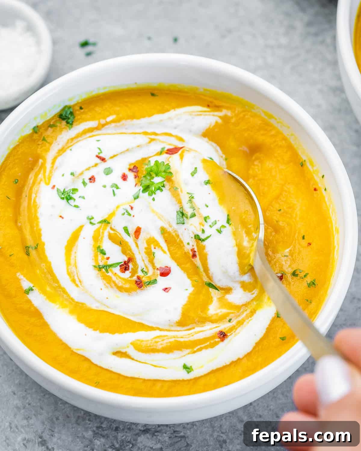 Golden Carrot Ginger Velouté 2 A white bowl of homemade carrot ginger soup swirled with creamy yogurt and garnished with fresh herbs or chili flakes.