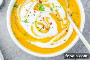 Carrot ginger soup in a bowl topped with yogurt and garnishes.