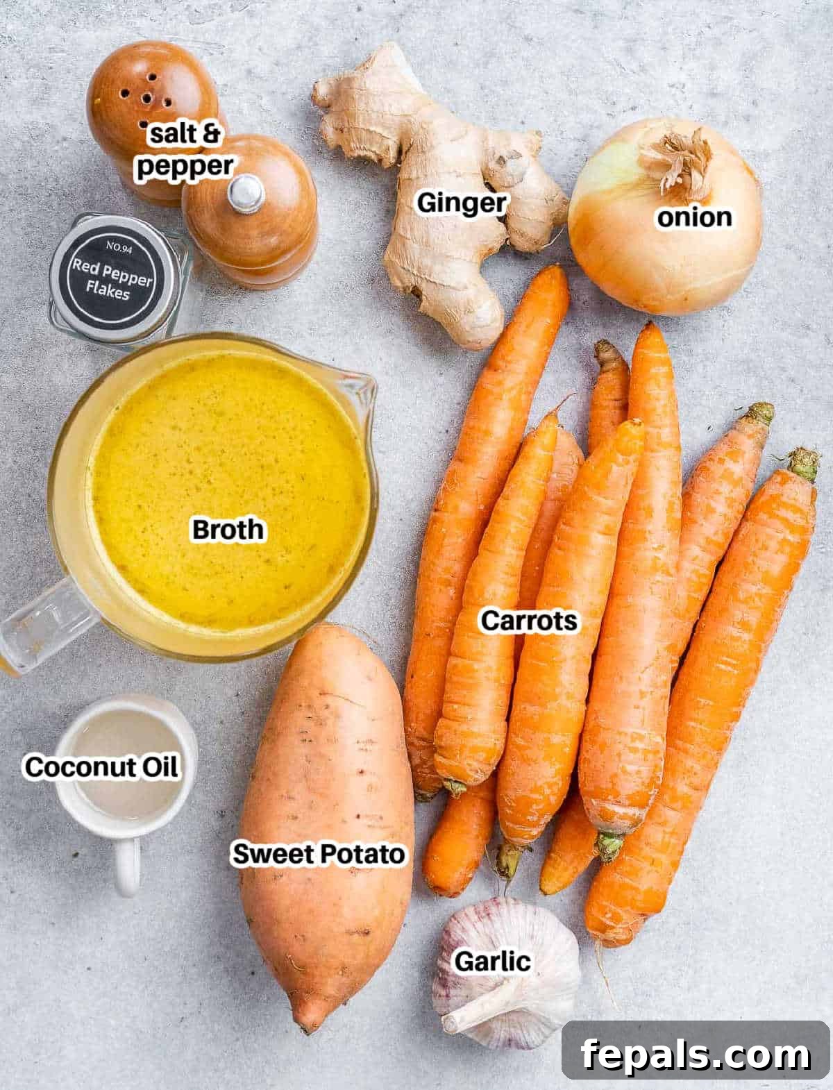 Golden Carrot Ginger Velouté 3 Fresh ingredients for carrot ginger soup laid out on a wooden board: coconut oil, sweet onion, garlic cloves, fresh ginger, carrots, sweet potato, and seasonings.