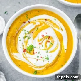 carrot soup in a round bowl topped with sour cream swirls and chili flakes.