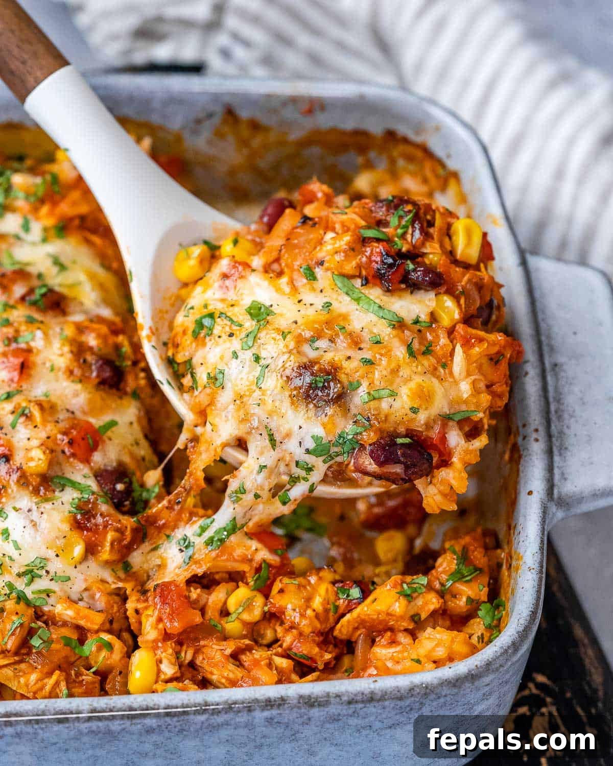 Close-up of a cheesy Mexican chicken casserole in a white baking dish, showing the bubbly, golden-brown cheese and rich filling.