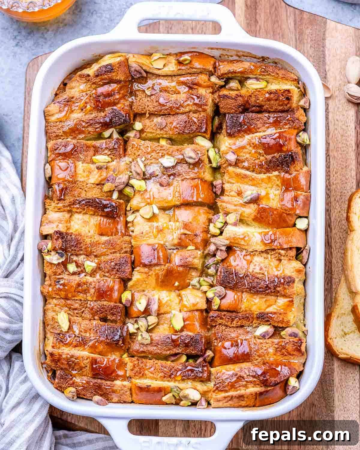 Baked Brioche French Toast Casserole in a white baking dish, golden brown on top with chopped pistachios scattered throughout.
