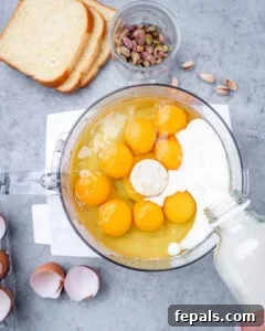 Food processor filled with blended pistachio mixture, with eggs and milk added on top before mixing into a custard.
