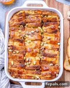 Baked Brioche French Toast Casserole in a white baking dish, golden brown on top with chopped pistachios scattered throughout.