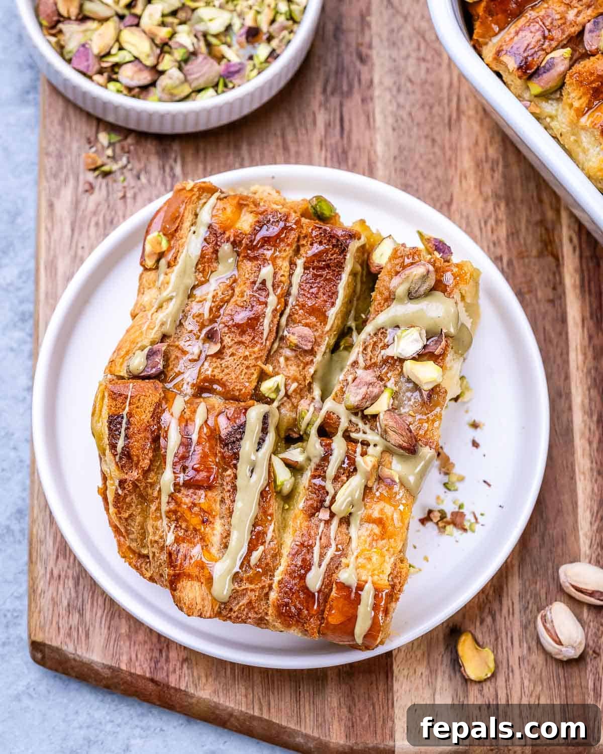 Slice of Brioche French Toast Casserole on a white plate, drizzled with pistachio butter and topped with crushed pistachios.
