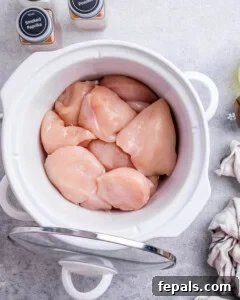Effortless Slow Cooker BBQ Pulled Chicken 13 Several raw boneless skinless chicken breasts placed in a white crockpot.