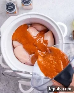 Effortless Slow Cooker BBQ Pulled Chicken 14 Homemade BBQ sauce being poured over raw chicken breasts inside a crockpot.