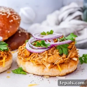 Effortless Slow Cooker BBQ Pulled Chicken 17 Open-faced bun loaded with BBQ shredded chicken and sliced red onion, with another sandwich in the background.