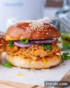 Effortless Slow Cooker BBQ Pulled Chicken 18 BBQ shredded chicken piled onto a sandwich bun with sesame seeds, topped with red onion and parsley.