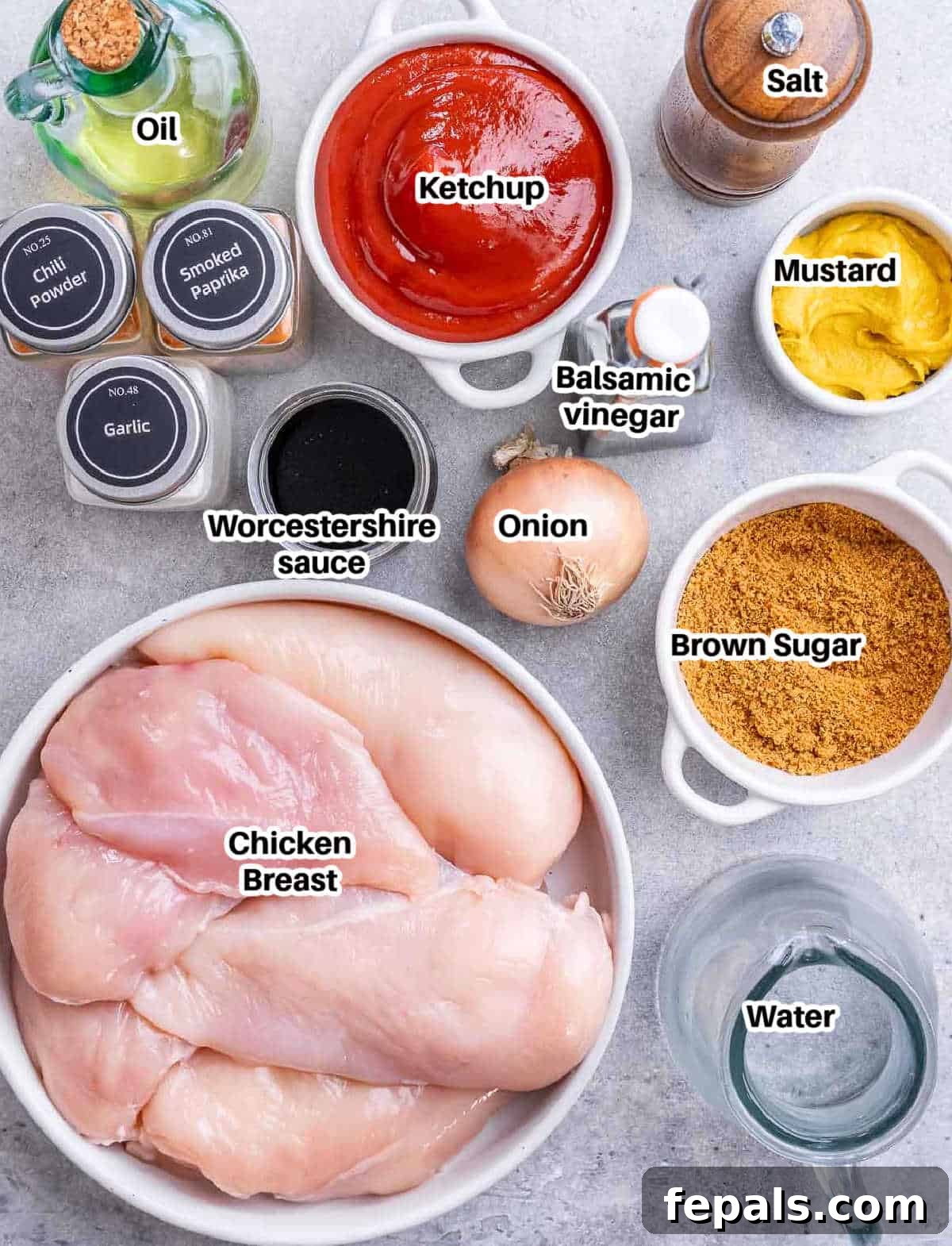Effortless Slow Cooker BBQ Pulled Chicken 3 A collection of ingredients laid out on a table, including chicken breasts, ketchup, onions, spices, and sauces, ready to make shredded BBQ chicken.