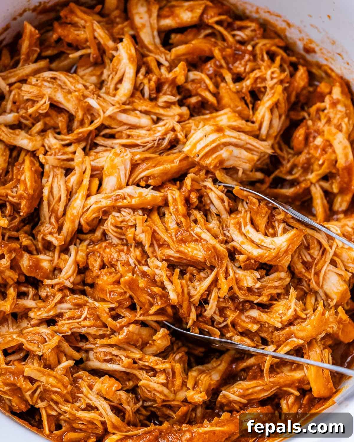 Effortless Slow Cooker BBQ Pulled Chicken 8 Juicy shredded BBQ chicken simmering in its rich sauce inside a crockpot, with metal tongs ready to serve.