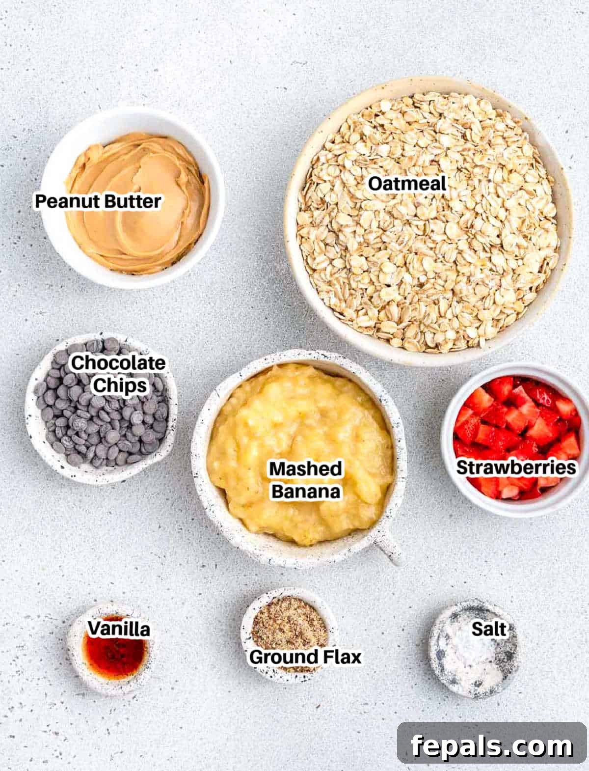 A collection of ingredients for strawberry oatmeal cookies, including oats, bananas, strawberries, and peanut butter.