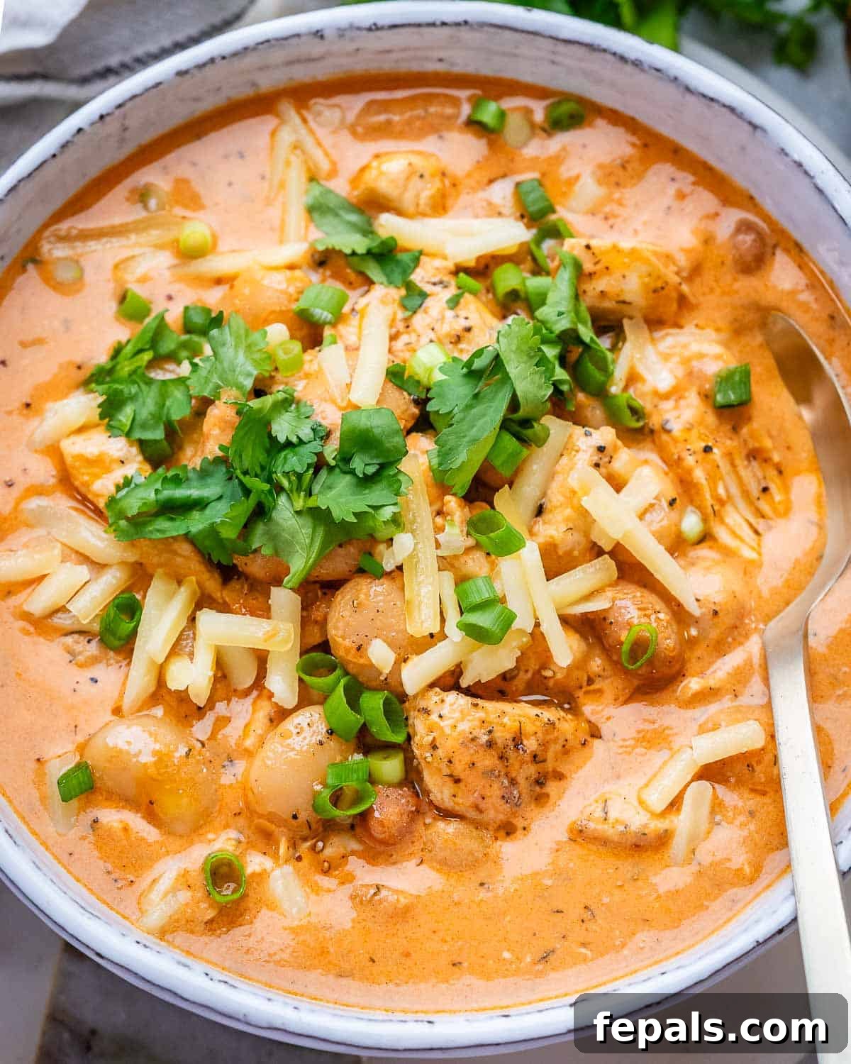 A white bowl of creamy crack chicken chili on a marble board, garnished with fresh cilantro and shredded cheese.