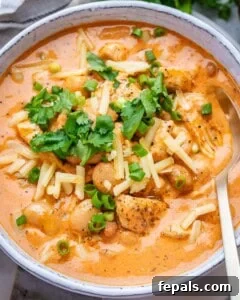 A white bowl of creamy crack chicken chili on a marble board, garnished with fresh cilantro and shredded cheese.