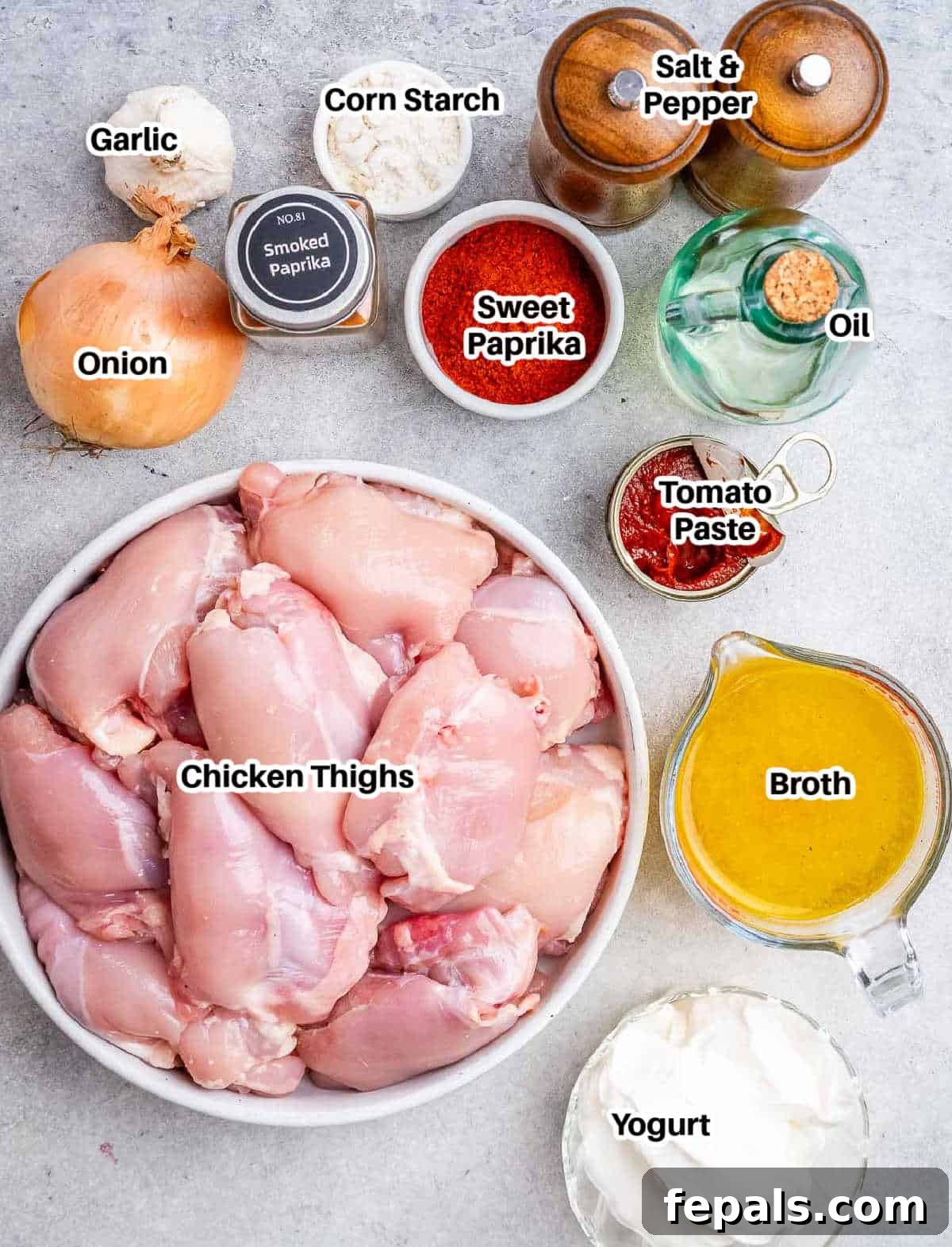 Creamy Hungarian Chicken 3 A flat lay photograph of all ingredients needed to make chicken paprikash, including chicken thighs, various paprikas, onion, garlic, and cream arranged neatly on a surface.