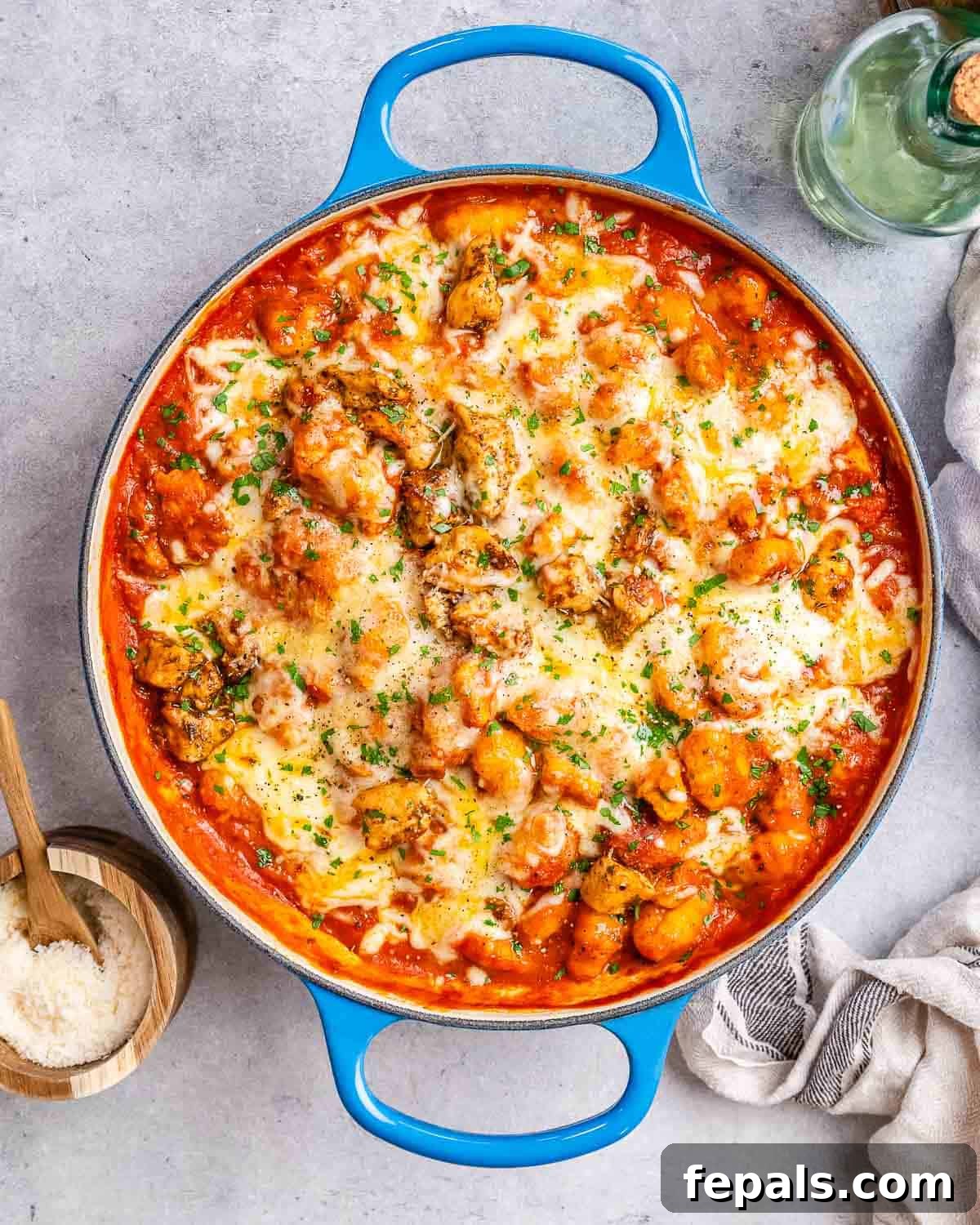 A blue skillet of creamy chicken gnocchi on a grey worktop, garnished with fresh herbs.