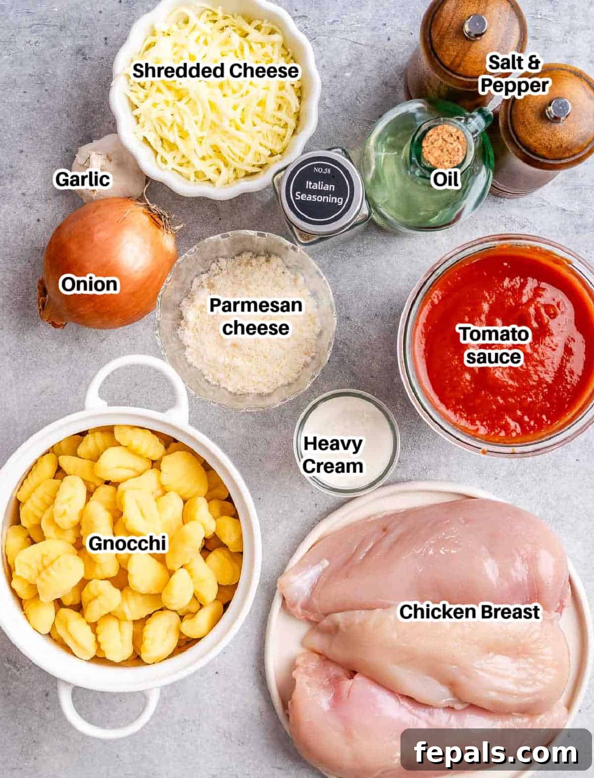 A flat lay of fresh ingredients including chicken, gnocchi, tomatoes, onion, garlic, and herbs to make chicken and gnocchi.