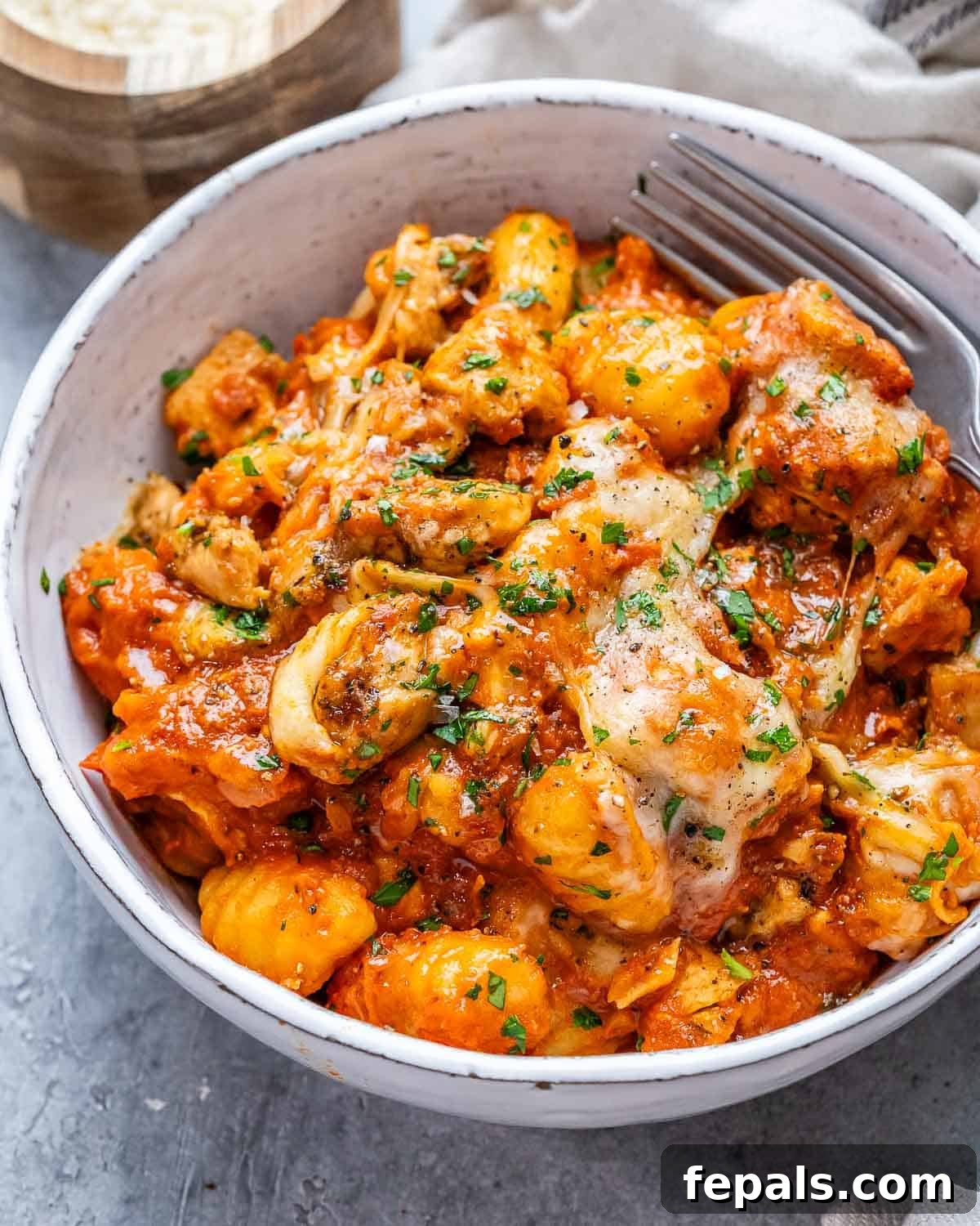 A close-up shot of a bowl filled with creamy chicken and gnocchi, topped with fresh basil.