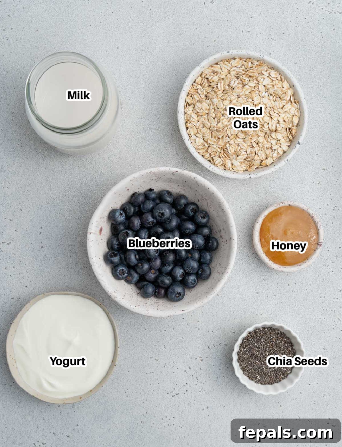 Easy Blueberry Overnight Oats 3 A vibrant flat lay showing all the fresh ingredients needed for making delicious blueberry overnight oats, including rolled oats, milk, yogurt, blueberries, chia seeds, and honey.