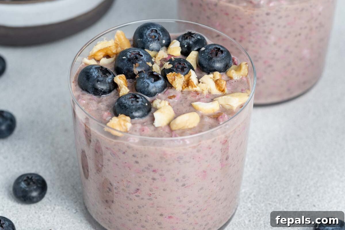 Easy Blueberry Overnight Oats 7 A glass cup filled with luscious blueberry overnight oats, garnished with a handful of fresh blueberries and a few mint leaves, ready for a healthy meal.