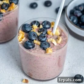 A cup with blueberry oatmeal topped with fresh blueberries and walnuts.