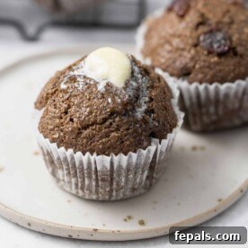 A close-up side shot of a single healthy bran muffin on a white plate, elegantly topped with a small square of melting butter.