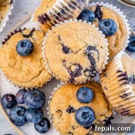 Top view of several fluffy blueberry muffins arranged on a white plate, showcasing their golden tops and visible blueberries.