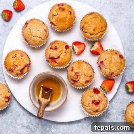 Top view of freshly baked strawberry muffins on a white plate, with a small bowl of honey for drizzling on the side.