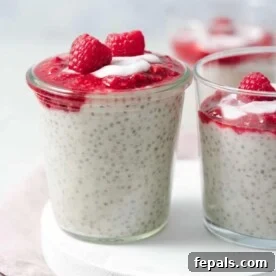Side view of a glass jar filled with creamy Greek yogurt chia pudding, generously topped with vibrant mashed raspberries, ready to be enjoyed.