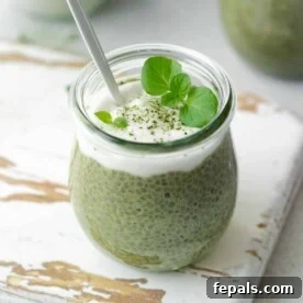 Side view of a glass jar filled with vibrant green matcha chia pudding, beautifully topped with a dollop of creamy coconut yogurt and a spoon resting inside.