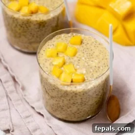 A glass cup of vibrant mango chia pudding, generously topped with finely chopped fresh mango pieces, offering a tropical delight.