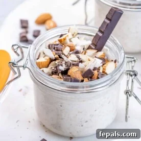 A side shot of inviting almond joy overnight oats in a jar, generously topped with shaved chocolate, crunchy almonds, and delicate coconut flakes.