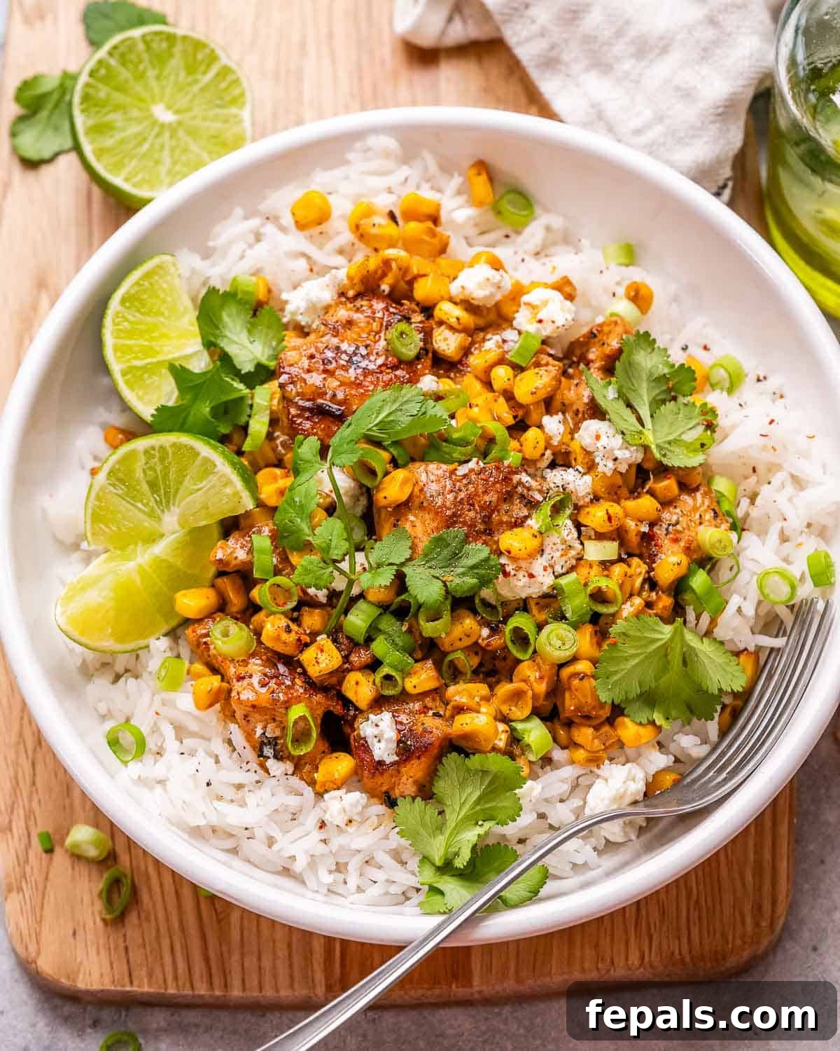 A round white bowl filled with fluffy white rice, topped generously with chunks of perfectly seared chicken breast, and a vibrant, creamy street corn salad, garnished with fresh cilantro.