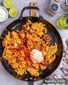 seasonings, sour cream, and mayo added to the chicken and corn in a pan.