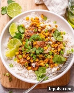 a round white bowl with rice topped with seared chicken breast chunks and street corn salad.