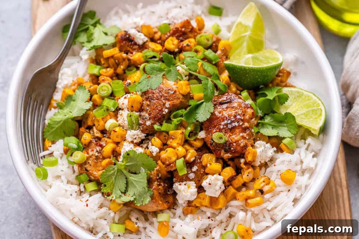A vibrant Street Corn Chicken Rice Bowl garnished with fresh cilantro and lime wedges, showcasing the creamy corn and seared chicken over fluffy rice.