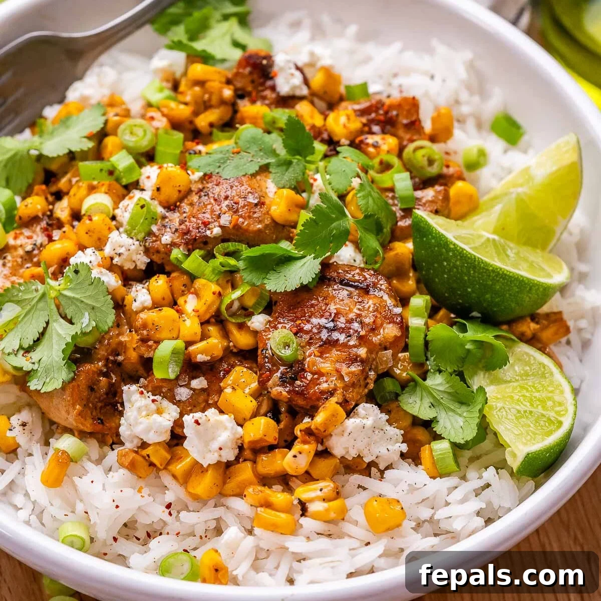A close-up shot of a beautifully arranged rice bowl, featuring seared chicken mixed with creamy street corn salad, garnished with cilantro.