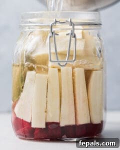 The pickling brine is being poured into a jar filled with turnips, ensuring they are fully submerged.