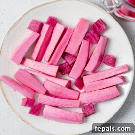 Top view of vibrant pink pickled turnip sticks arranged on a white round plate, ready to be served.