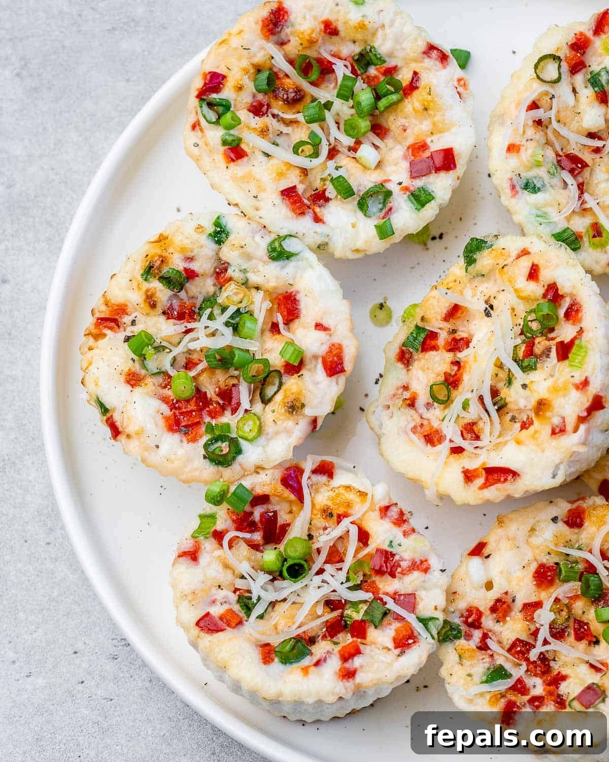 Close-up shot of egg white bites on a white plate, showing the fluffy texture and colorful veggie toppings.