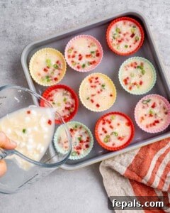 Muffin tin filled with unbaked egg white mixture, visible bits of red pepper and green onion floating on top.