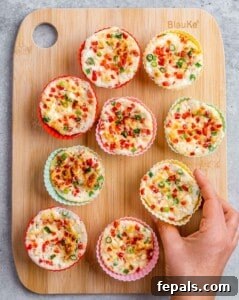 Hand placing a silicone muffin cup filled with egg white mixture onto a wooden board with other baked egg white bites.