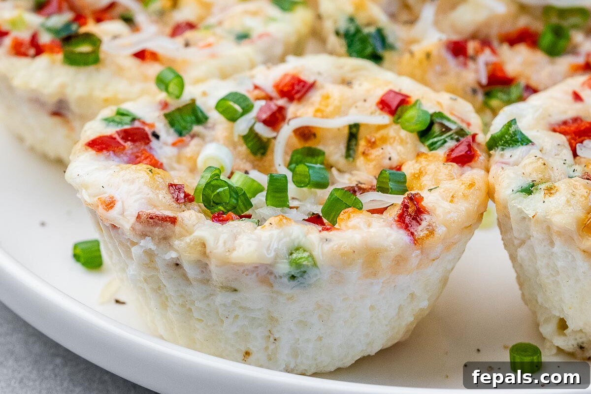 Side angle of a plate full of egg white bites, one slightly bitten to show the cheesy interior and airy texture.