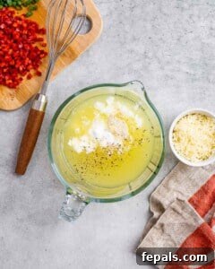 Overhead shot of a glass mixing bowl with egg whites, cottage cheese, and seasoning, surrounded by chopped red pepper and shredded cheese on a light surface.