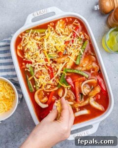 Process shot: Assembling the casserole by spooning the chicken and vegetable mixture over the rice base in a baking dish, then topping it with shredded Mexican cheese.