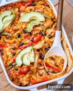 A finished chicken fajita casserole in a dish with a spoon, showing the perfectly cooked rice, chicken, and melted cheese, ready to be topped with avocado.